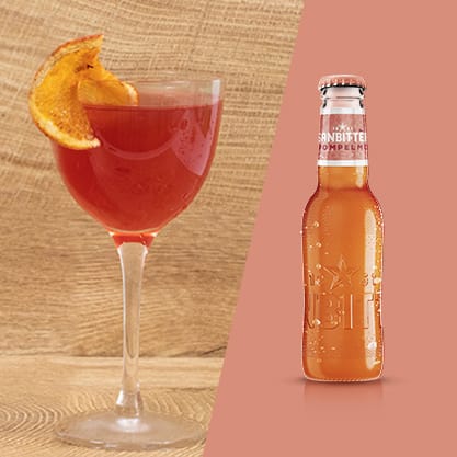 Cocktail rosso grapefruit bitter con vicino una bottiglie di Sanbittèr Emozioni Pompelmo