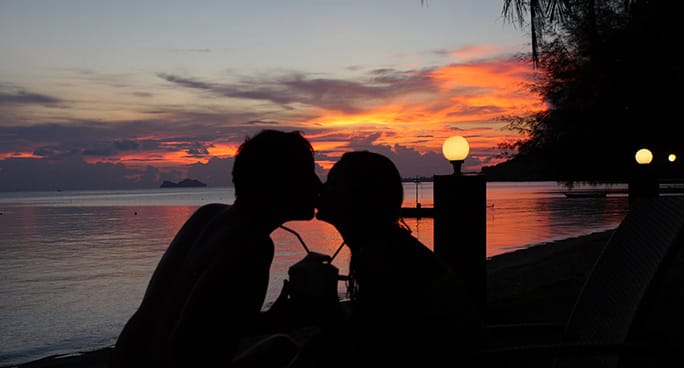 Una coppia si bacia in controluce al tramonto sul mare