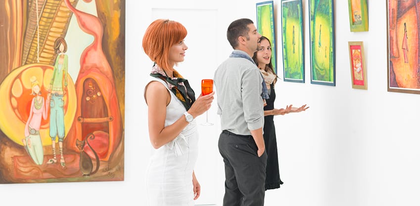 Scopri dove prendere un aperitivo al museo una donna con un drink mentre guarda alcuni quadri in un museo