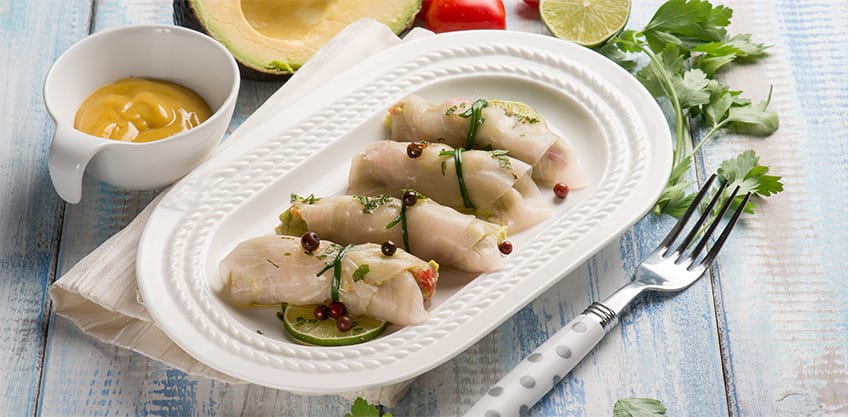 un piatto di involtini di pesce spada con vicino avocado e salse