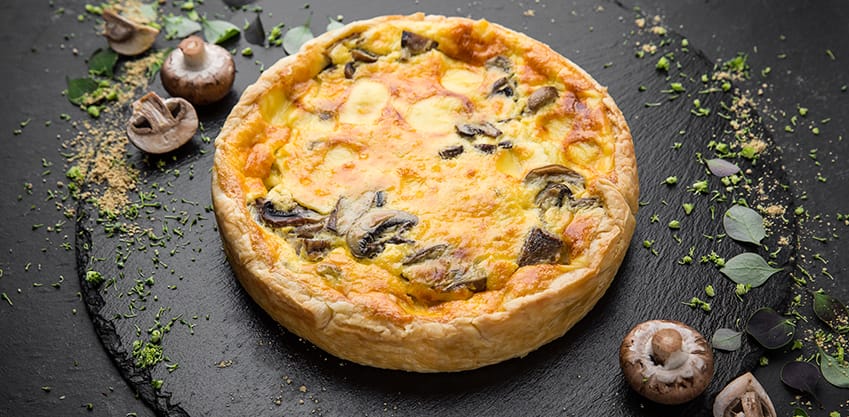 3 ricette per quiche da aperitivo gustose Quiche ai funghi su un piatto rotondo in ardesia
