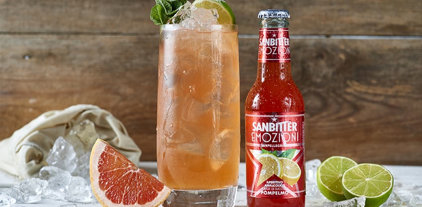 Bottiglia di Aperitivo Sanbittèr al pompelmo e bicchiere con succo di pompelmo, menta, lime e ghiaccio