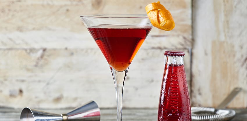 Cocktail rosso con una bottiglietta di Sanbittèr accanto