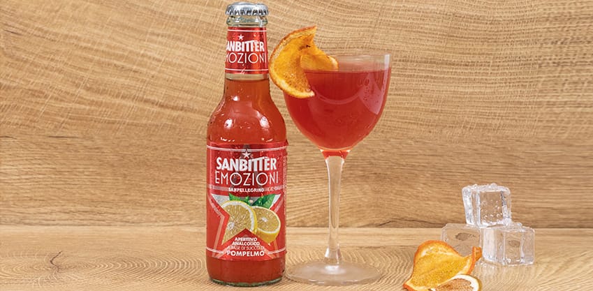 Scopri il cocktail al pompelmo Grapefruit Bitter! Cocktail rosso grapefruit bitter con vicino una bottiglie di Sanbittèr Emozioni Pompelmo