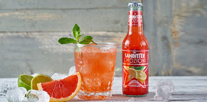 Bottiglia Sanbittèr al succo di pompelmo e bicchiere con cocktail pompelmo, menta, lime e ghiaccio